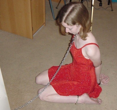 On her knees, chained and cuffed.